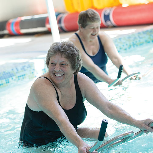 Two senior women ride aqua cycles for exercise in the Kroc pool.